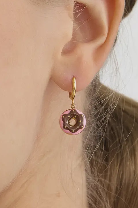 Close-up of an ear wearing a pink donut-shaped earring with gold accents.