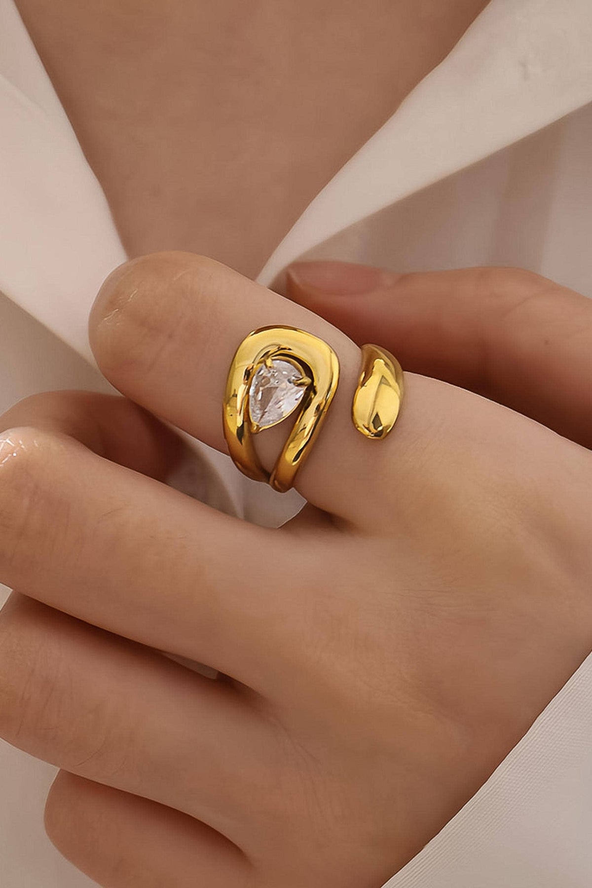 Gold ring with a clear gemstone on a hand against a neutral background
