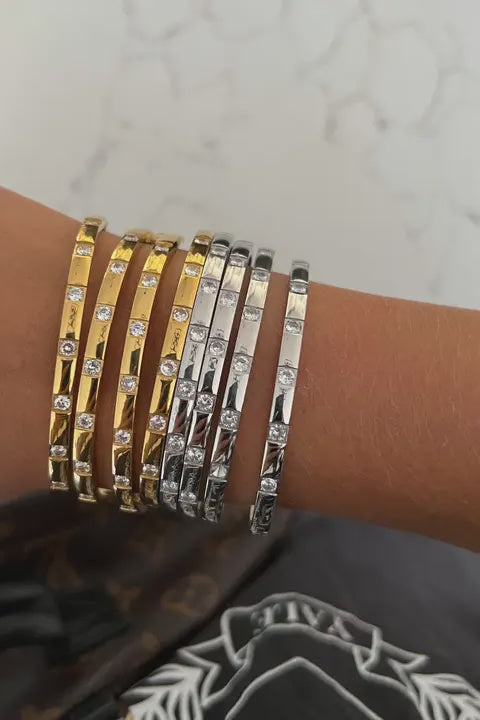 Wrist wearing gold and silver bracelets on a neutral background