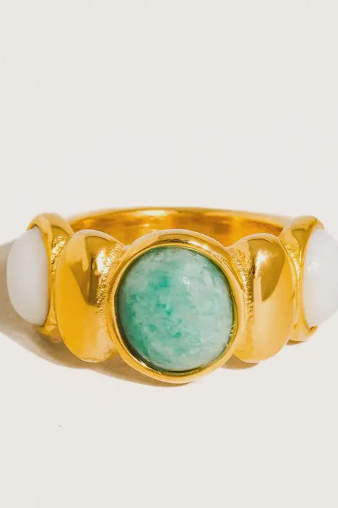 Gold ring with a green stone and two white stones on a light background