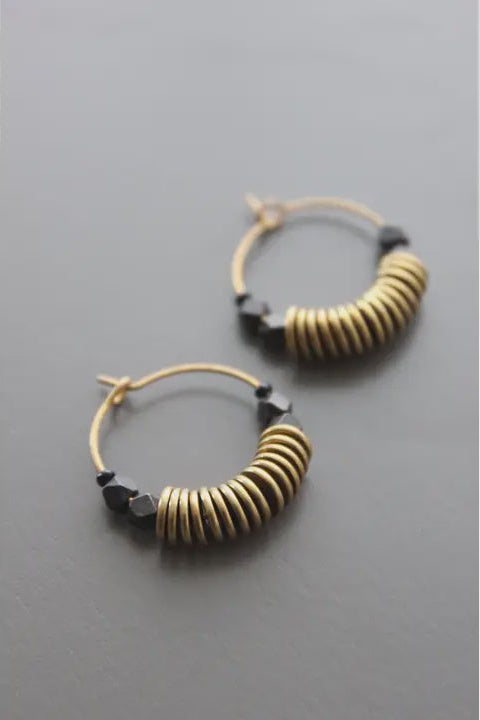 Pair of gold hoop earrings with black beads on a gray background