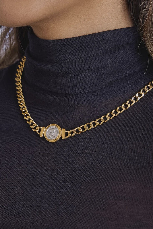 Gold chain necklace with a round pendant on a dark turtleneck