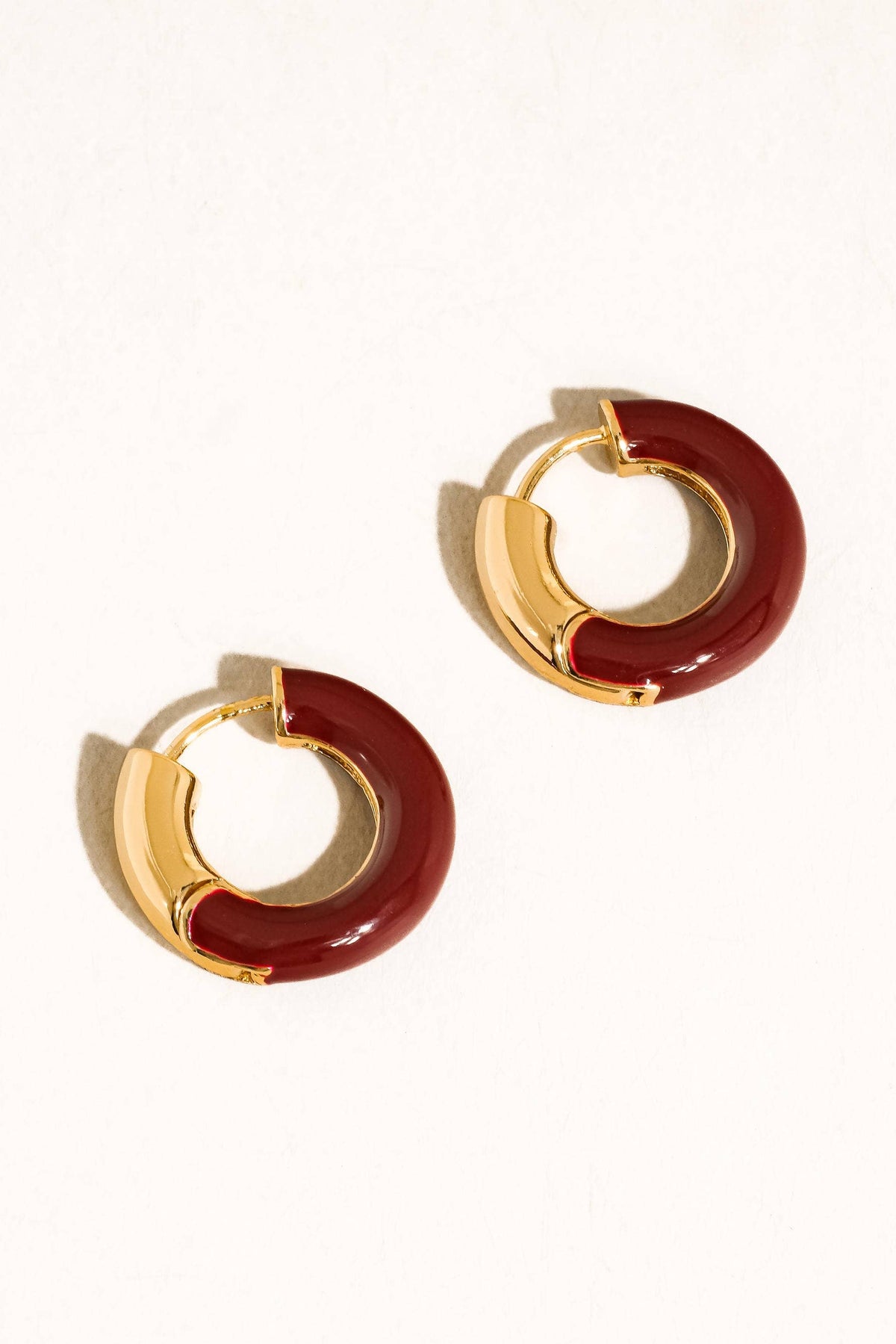 Pair of gold and red hoop earrings on a white background