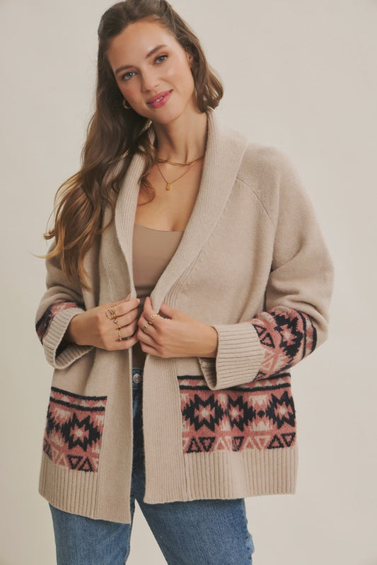 Woman wearing a beige cardigan with patterned sleeves on a plain background