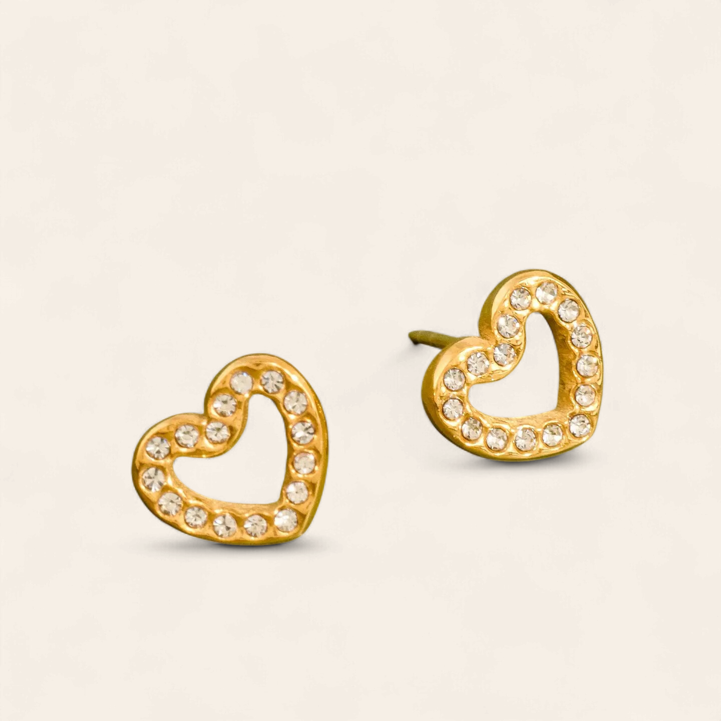 Gold heart-shaped earrings with clear stones on a beige background