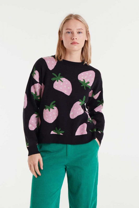 Person wearing a black sweater with pink strawberry pattern and green pants on a white background