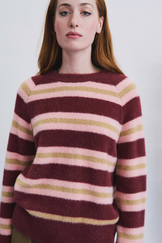 A woman wearing a fuzzy knit sweater with horizontal stripes in burgundy, light pink, and muted olive green, photographed against a plain light background.
