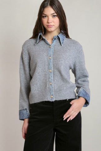 Woman wearing a gray sweater over a denim shirt with black pants on a plain background