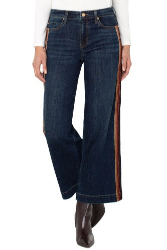 Dark blue jeans with brown side stripes worn by a person on a white background