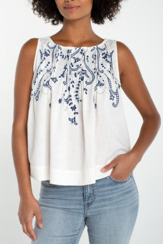Woman wearing a white sleeveless top with blue patterns and blue jeans on a white background