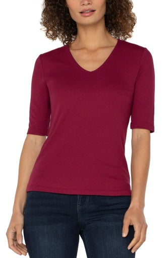 Woman wearing a maroon V-neck shirt with three-quarter sleeves on a white background