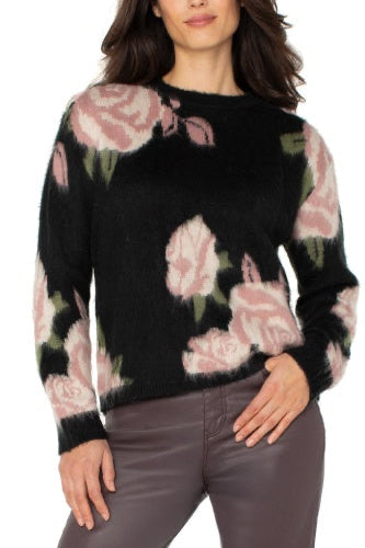 Woman wearing a black sweater with pink floral patterns on a white background