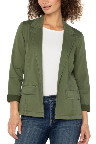 Woman wearing an olive green jacket over a white shirt and blue jeans on a white background