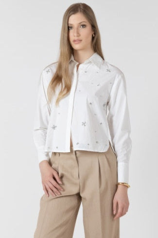 Woman wearing a white blouse with floral patterns and beige pants on a white background