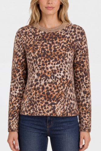 A woman wearing a long-sleeve crewneck sweater with a brown, beige, and black leopard print pattern, paired with dark blue jeans, against a plain white background.
