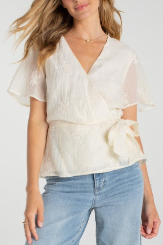 Woman wearing a white blouse with ruffled sleeves and blue jeans on a white background