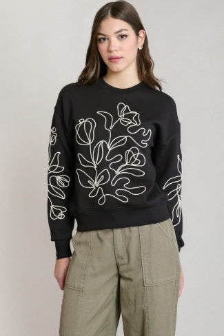 Person wearing a black sweater with white floral patterns on a plain background