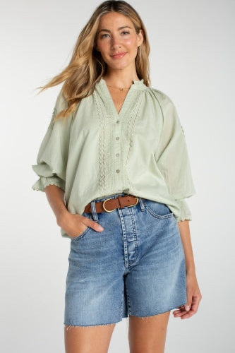 Woman wearing a light green blouse and denim shorts on a white background