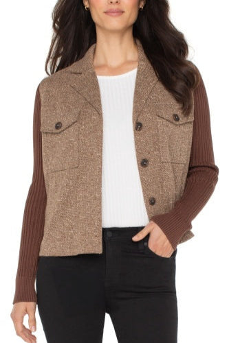 Woman wearing a brown and beige patterned cardigan over a white shirt and black pants on a white background