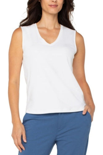 Woman wearing a white sleeveless top and blue pants on a white background