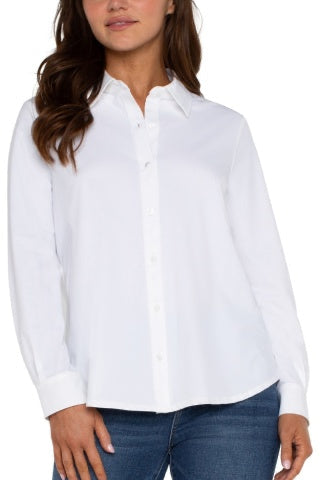 A woman wearing a white long-sleeve button-up shirt with a pointed collar and blue jeans, shown from the chest down against a plain white background.