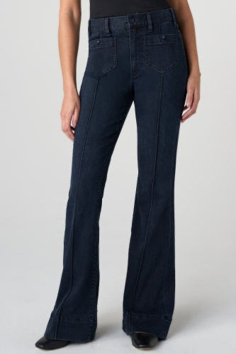 A model wearing a pair of dark navy blue high-waisted flare jeans with front pleats, shown from the waist down against a light gray studio background.