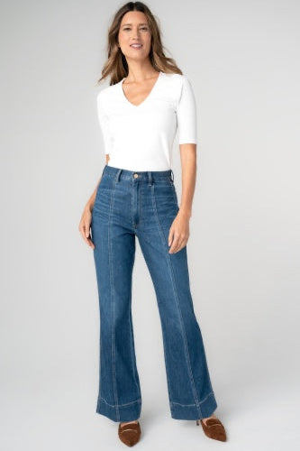 Woman wearing a white top and blue jeans on a plain background