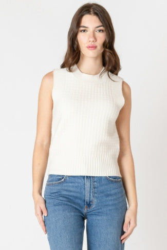Woman wearing a sleeveless cream top and blue jeans on a white background
