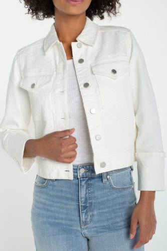 Person wearing a white denim jacket and light blue jeans on a plain background