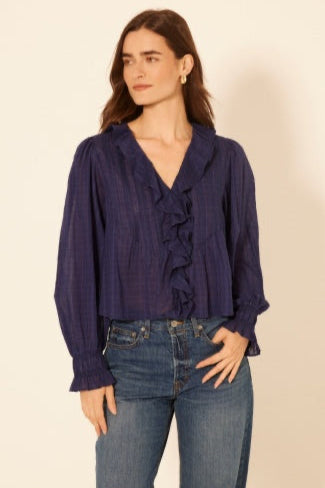 Woman wearing a navy blue blouse with ruffles and jeans on a beige background