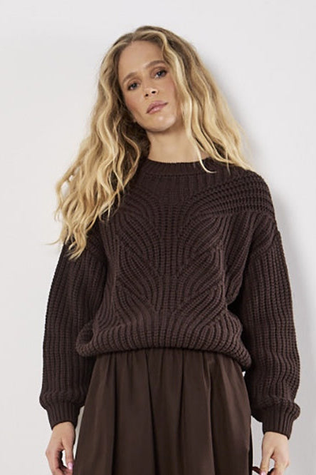 Woman wearing a brown knitted sweater and skirt against a white background