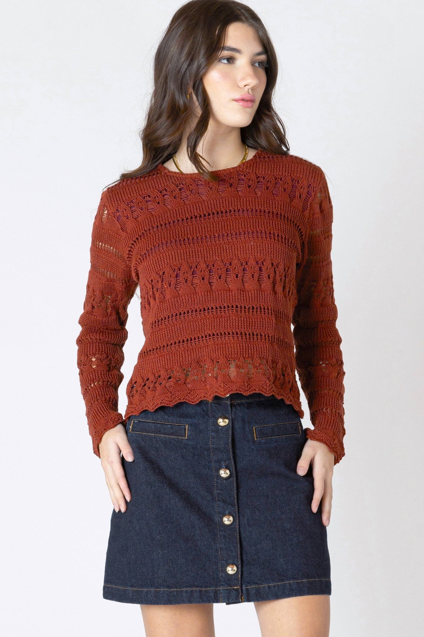 Woman wearing a rust-colored sweater and denim skirt on a white background