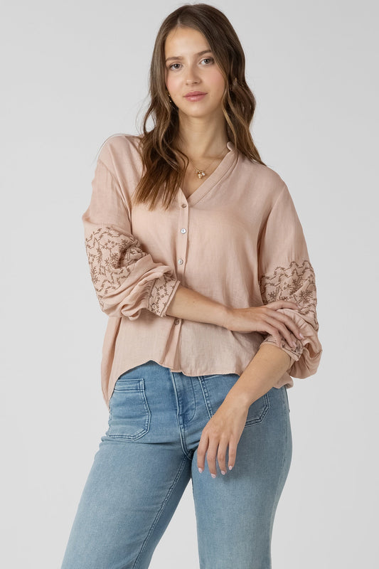 Woman wearing a light pink blouse with lace sleeves and blue jeans on a white background